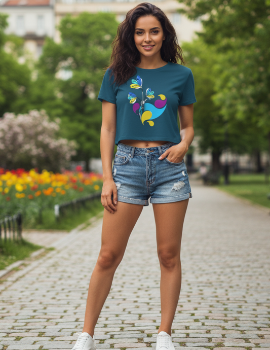 Woman wearing a teal t-shirt with a colorful design and denim shorts standing in a park.